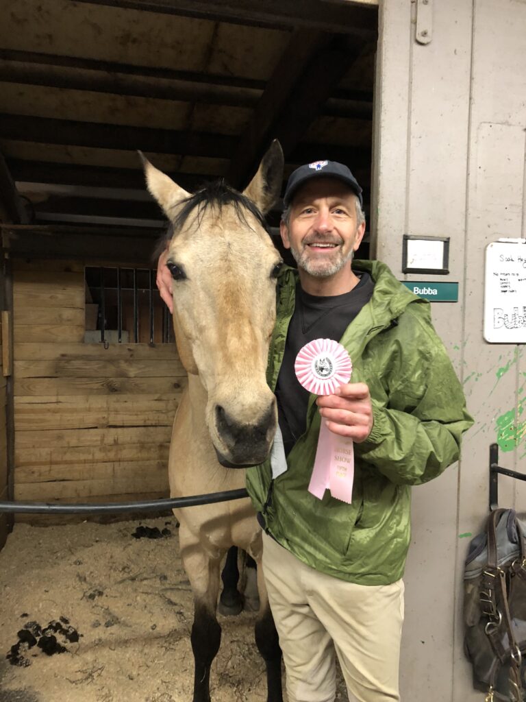 Man  with a white horse after receiving a ribbon during a horse show 